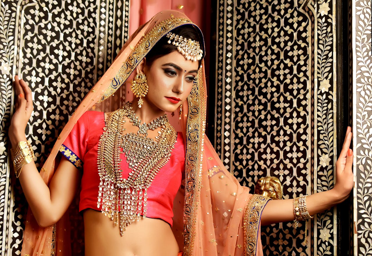 A beautiful woman in traditional Indian clothing and jewelry posing against an ornate background.